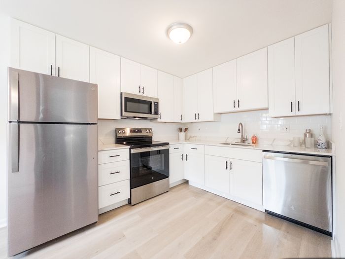 Bright kitchen with stainless steel appliances and white cabinets at College Arms Apartments.
