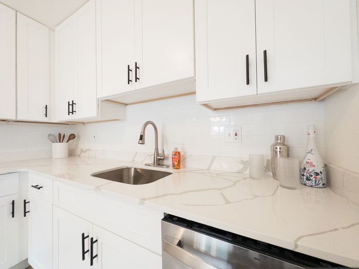Bright white kitchen at College Arms Apartments with marble-look countertops, stainless sink, and subway tile backsplash.