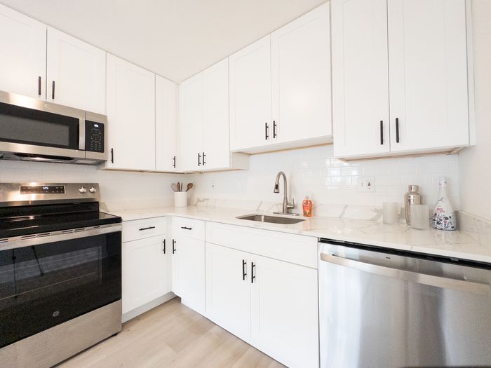 Modern white kitchen at College Arms Apartments with white cabinets, stainless steel appliances, and quartz countertops.