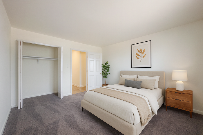 Spacious furnished bedroom with bed, nightstand, lamp and open closet at College Arms Apartments in Collegeville, PA.