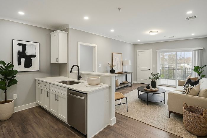 Bright, modern living room with cozy seating, stylish decor, and an open kitchen featuring elegant cabinetry and a sleek sink. Sunlit space with large windows and contemporary furnishings.