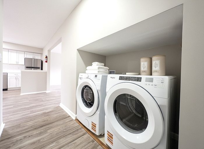 Chic apartment interior featuring a modern laundry nook with washer and dryer, complementing a bright, open-concept kitchen with sleek appliances and wood-style flooring.