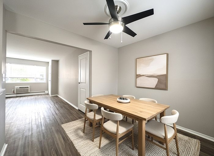 Elegant dining room with a modern ceiling fan, wooden table, and stylish seating, leading into a sunlit living area with sleek flooring.