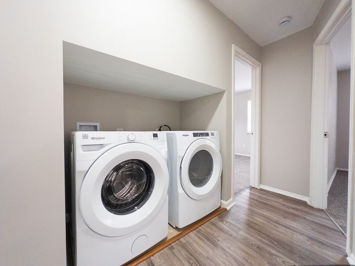 Modern apartment hallway featuring a sleek in-unit laundry area with Whirlpool washer and dryer, complemented by elegant wood flooring.