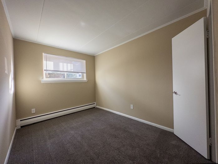 Inviting bedroom with neutral tones, plush carpeting, and ample natural light through a wide window.