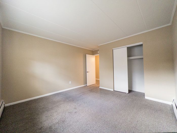 Bright, spacious room with neutral tones, featuring a plush carpet and a white closet, perfect for customization and comfort.