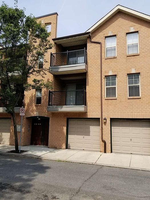 Charming brick apartment building featuring double garages and balcony, nestled in a serene neighborhood with lush greenery.