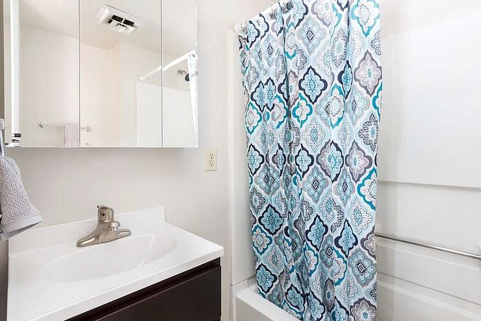 Bright bathroom featuring modern vanity with sleek faucet, mirrored cabinets, and a stylish blue pattern shower curtain.