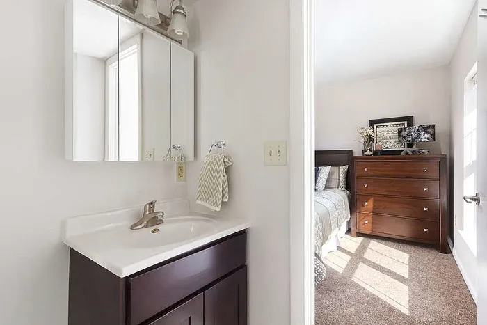 Bright bathroom with elegant vanity leading to a cozy bedroom featuring a stylish dresser and natural light.