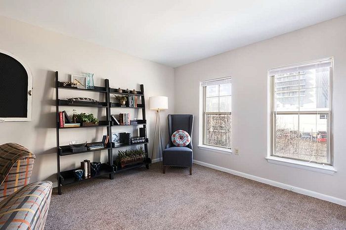 Bright and inviting living area with large windows, cozy armchair, and sleek shelving unit perfect for modern city living.