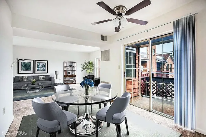 Bright and inviting living area with modern glass dining table, elegant gray chairs, and large sliding doors leading to a cozy balcony.