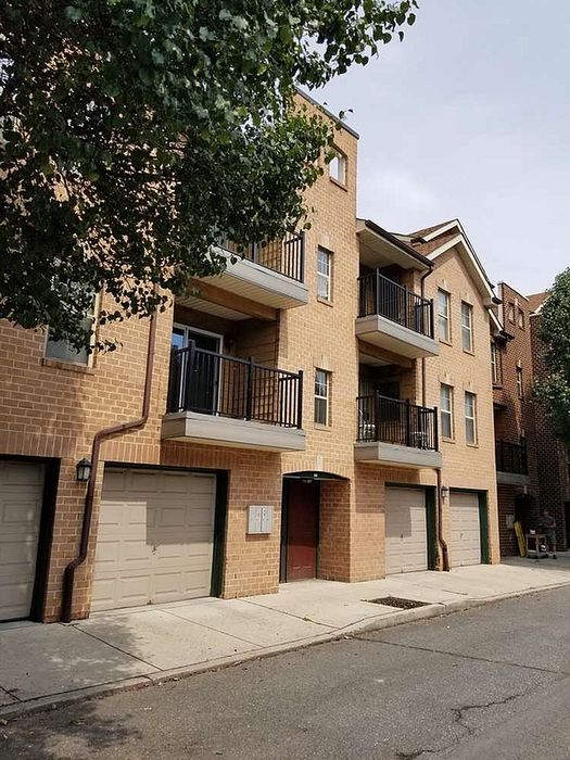 Charming brick apartment building with private balconies and secure garages, nestled in serene surroundings.
