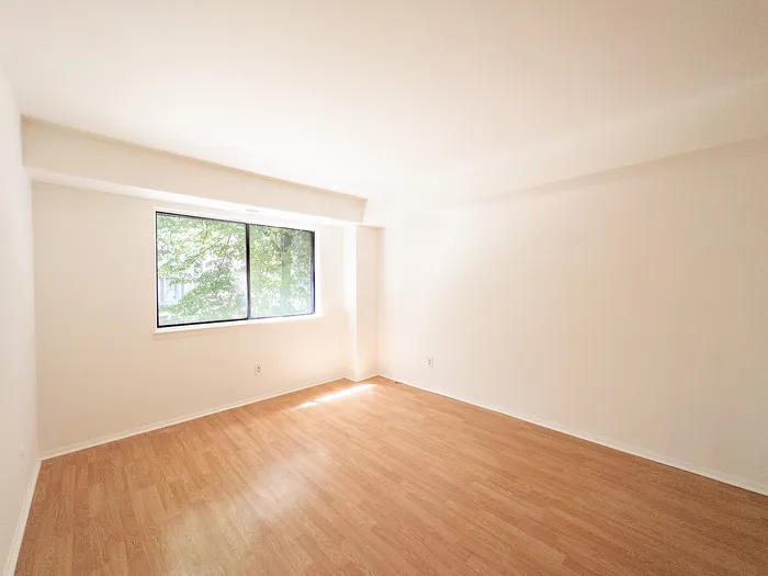 Bright and airy room with large window, showcasing modern hardwood floors and abundant natural light.