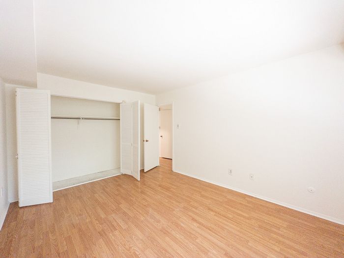 Bright and spacious bedroom featuring elegant hardwood flooring, ample closet space, and fresh white walls, ready for personalization.