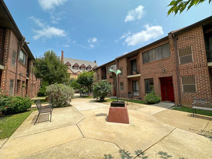 Charming courtyard view of a quaint brick apartment complex with lush greenery and inviting benches, perfect for relaxation.