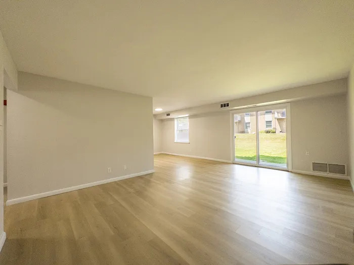 Spacious living area with elegant wooden flooring and large windows offering abundant natural light and garden views.
