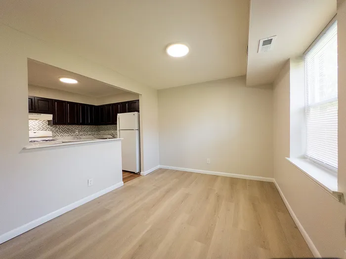 Bright open-plan dining area with elegant wood flooring, adjacent to a modern kitchen featuring sleek dark cabinets and a stylish backsplash.
