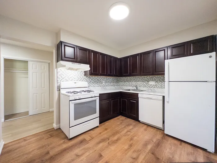 Modern apartment kitchen with rich dark wood cabinets, elegant tile backsplash, and sleek white appliances.