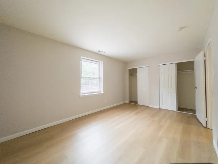 Bright and spacious bedroom with sleek wooden floors, ample closet space, and a large window inviting natural light.