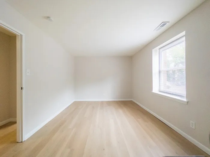 Bright and airy room with large window, modern hardwood flooring, and neutral walls, perfect for personalization.