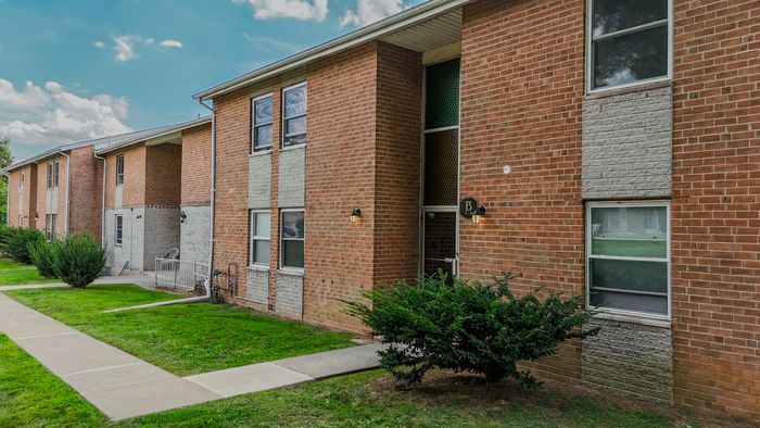 Charming brick apartment building with lush green lawn and cozy entrance, offering a welcoming suburban living experience.