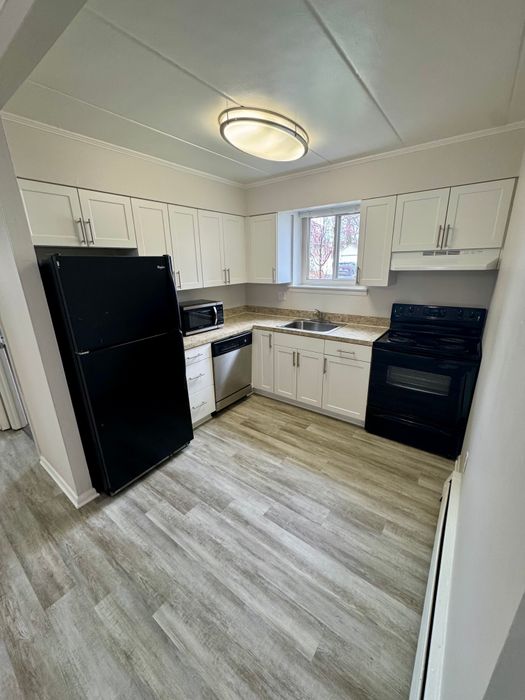 Modern kitchen with sleek black appliances, ample white cabinetry, and hardwood flooring.
