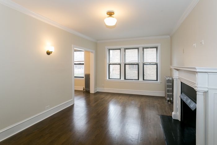 A living room with dark hardwood floors, sunny windows, and a neutral color palette.