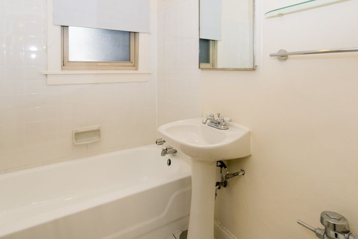 A bathroom with a white pedestal sink, medicine cabinet, and a bathtub.