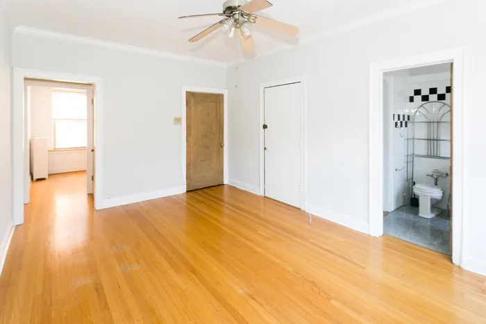 A bright and sunny living room with hardwood floors, light grey walls, and a ceiling fan.