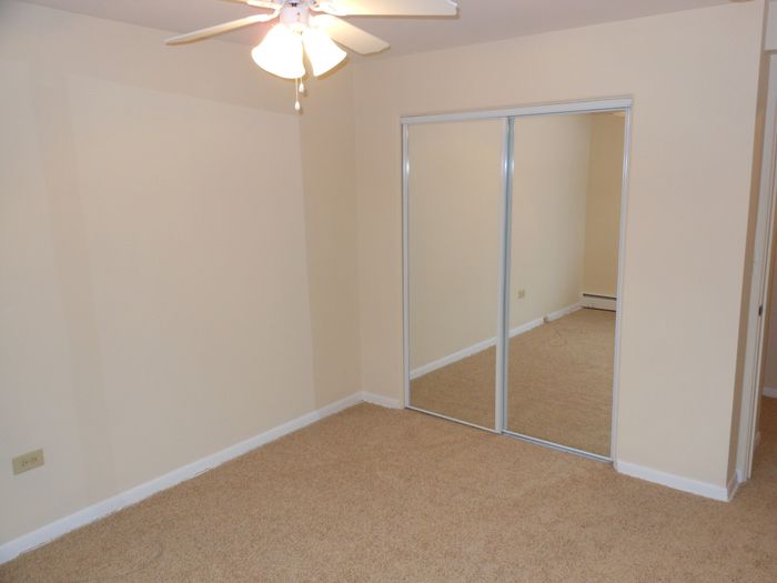 A bedroom with good closet space, wall to wall carpeting, and a ceiling fan.