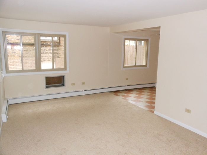Living room with a thru wall air conditioner and beige wall to wall carpeting.