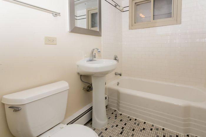 A bathroom with a white pedestal sink, black and white checkered tile floor, and a white bathtub.