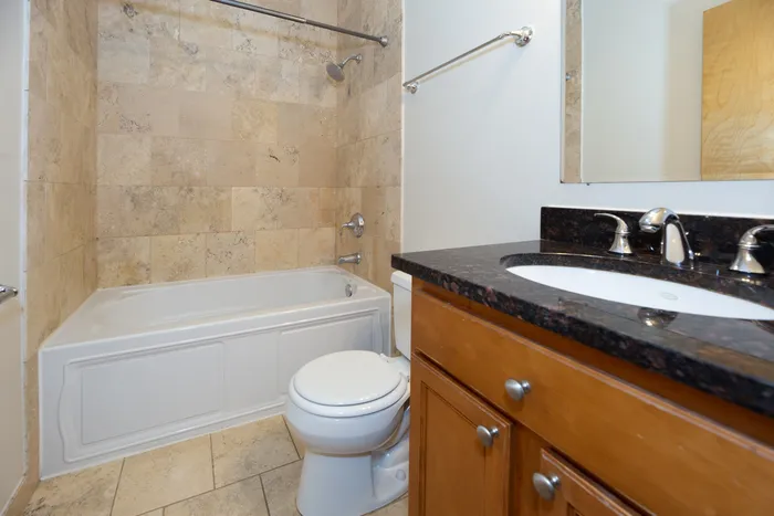 Updated bathroom featuring a wooden vanity with granite top and a white bathtub.