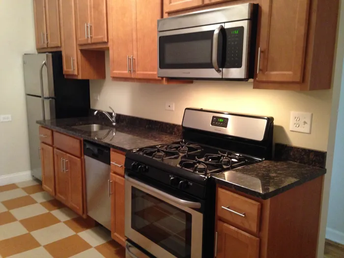 A kitchen with wood cabinets, stainless steel appliances including a microwave and dishwasher, with dark granite countertops.