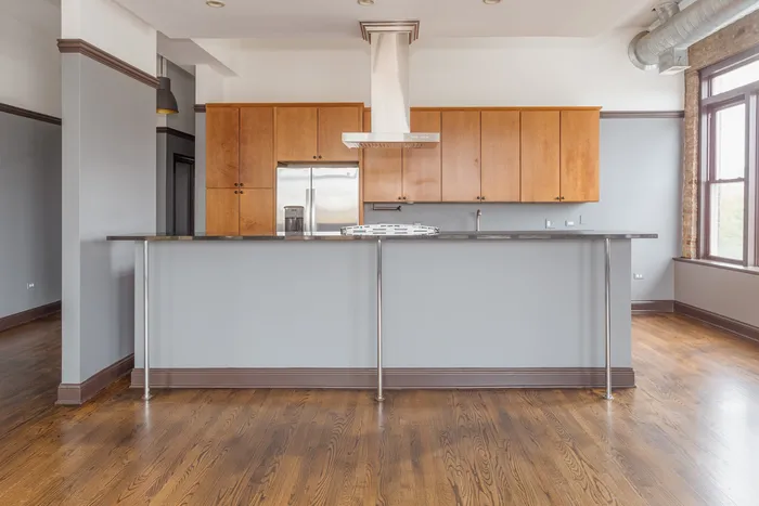 An open concept kitchen with light wooden cabinets, stainless steel appliances including a dishwasher, and a hood over the cook top.