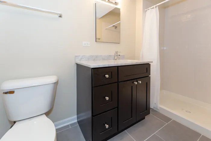 Updated bathroom with a dark wood vanity, granite top, and a walk in shower.