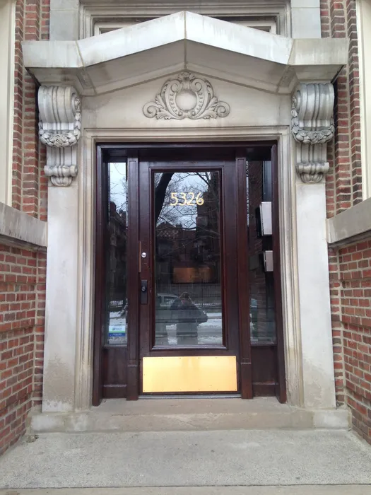 The elegant main entrance with a wood and glass door, intercom access, and carved stone pediment.