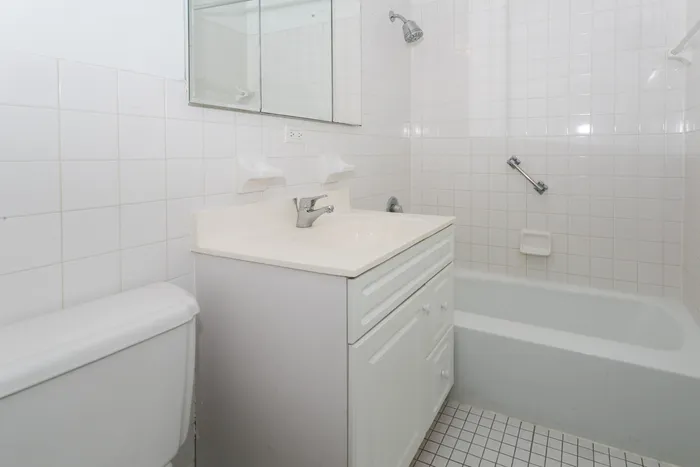 Bathroom with white vanity, white tiles, and a bathtub.