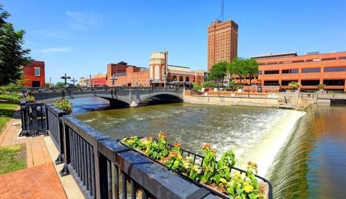 A large river flowing next to the property with brick buildings in the background in downtown Aurora.