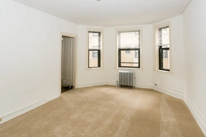 A studio apartment with carpeted living room, sunny windows and a neutral beige color palette.