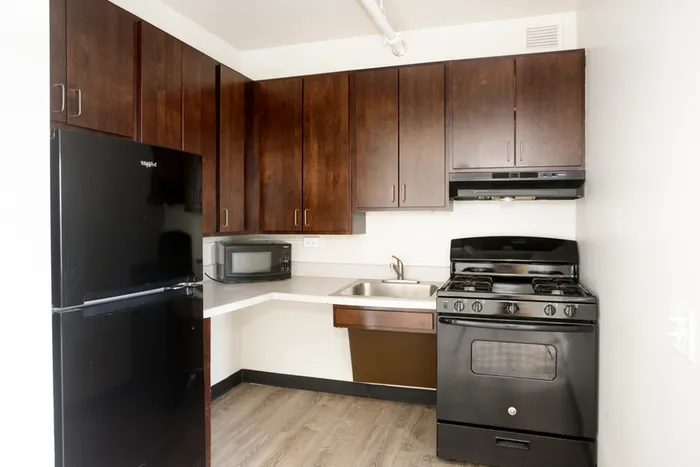 Kitchen area with dark wood cabinets, black appliances a roll unider sink and countertop