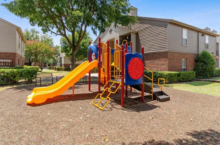 PlaygBright playground surrounded by trees and greenery at a Plano, TX apartment community.round