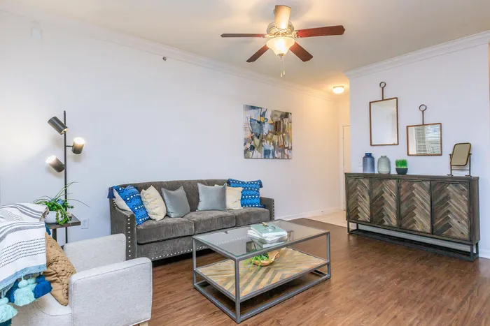 a cozy living room with a couch, arm chair, coffee table, wooden floors, and a ceiling fan
