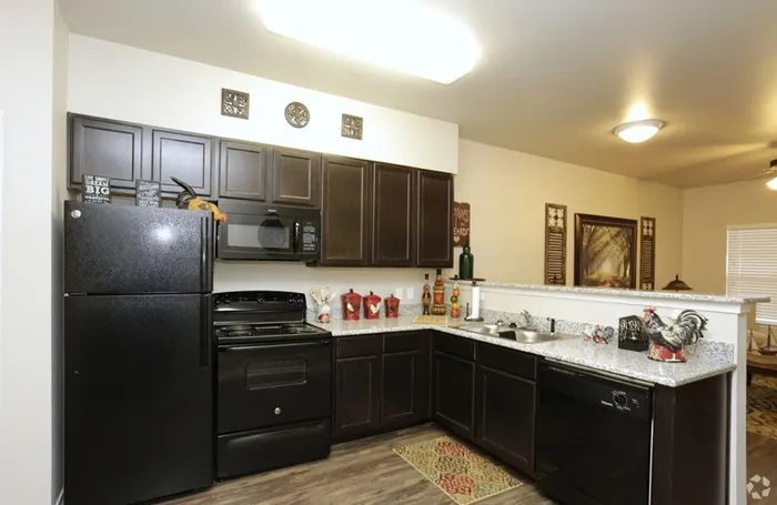 Modern kitchen with dark wood cabinetry, granite countertops, and black appliances at Arroyo Seco Villas in San Antonio, TX.