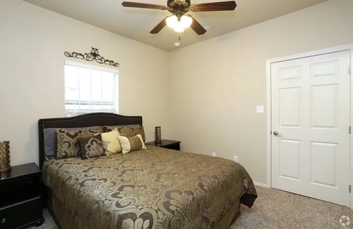 Elegant bedroom with a patterned bedspread, plush pillows, and a ceiling fan at Arroyo Seco Villas in San Antonio, TX.