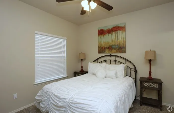 Bright bedroom with a classic metal bedframe, crisp white bedding, and warm decor at Arroyo Seco Villas in San Antonio, TX.