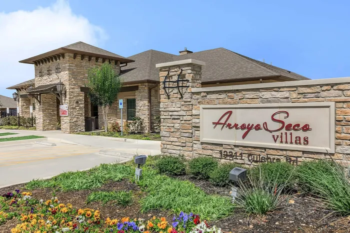 Beautiful stone exterior and welcoming signage at Arroyo Seco Villas in San Antonio, TX, surrounded by vibrant landscaping and flowers.