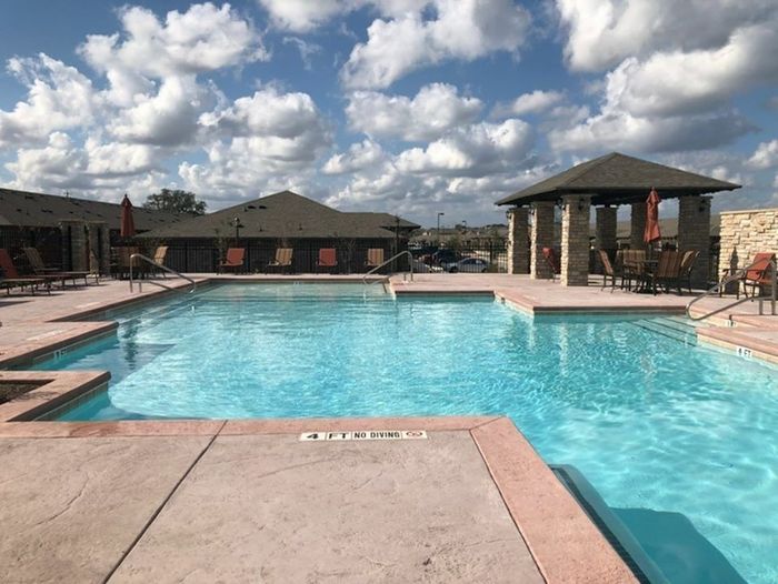 Resort-style swimming pool with sparkling blue water and ample lounge seating at Arroyo Seco Villas in San Antonio, TX.