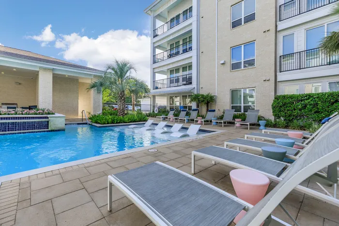 poolside seating overlooking a crisp blue swimming pool and four-story apartment building