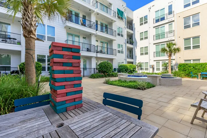 courtyard image focused on a table with a wooden stacking game, along with other tables, chairs, and a fountain in the background